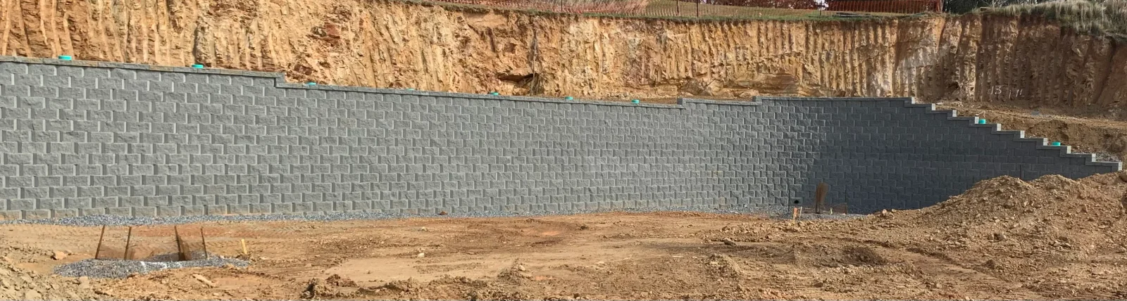 Gray segmental retaining wall blocks installed on sloped terrain with proper drainage