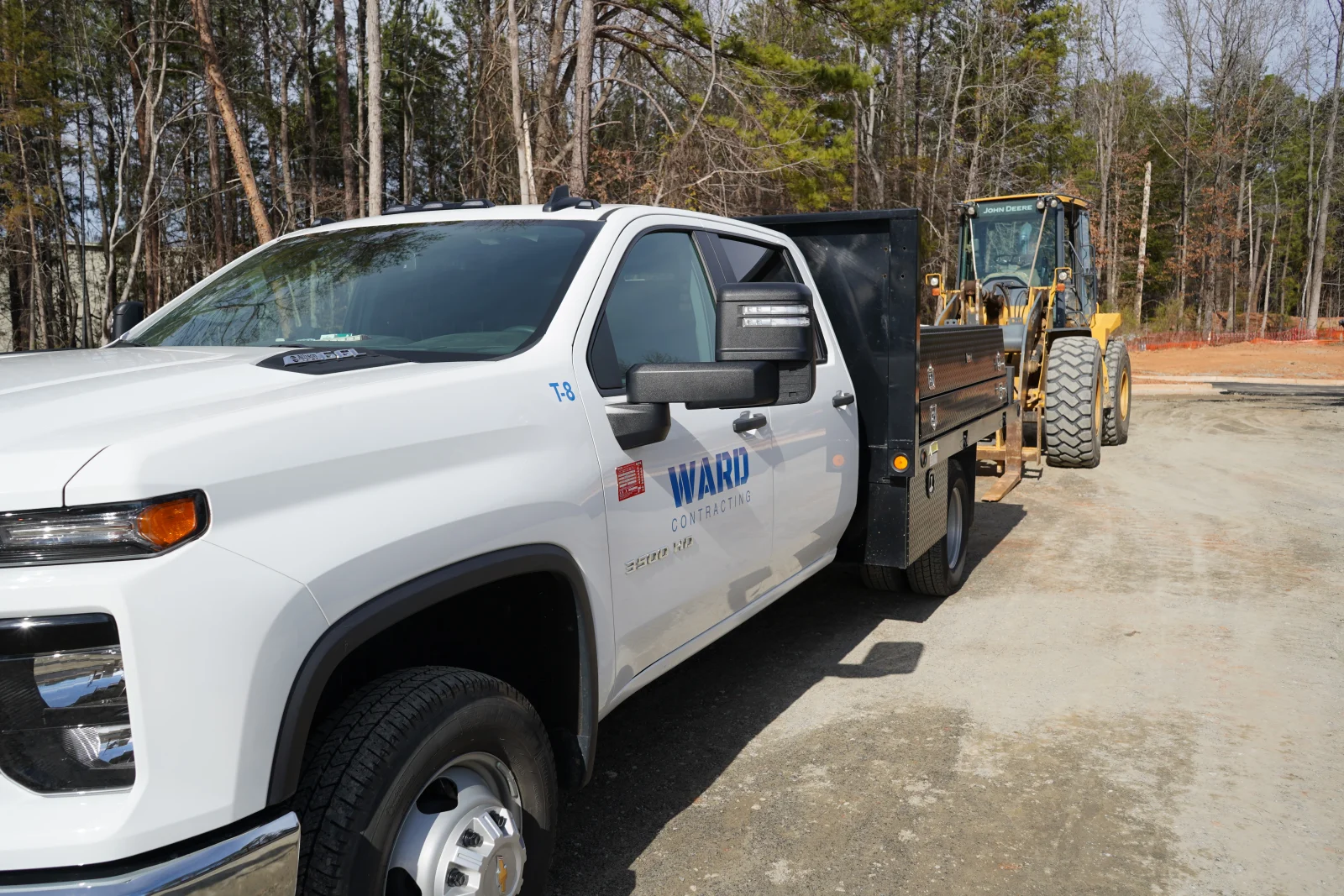 White pickup truck with flatbed and yellow wheel loader on gravel job site