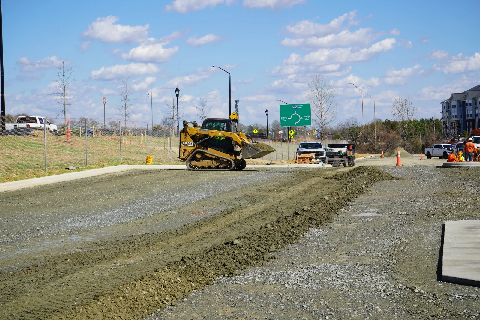 Tracked skid steer loader grading and compacting aggregate base course on commercial site