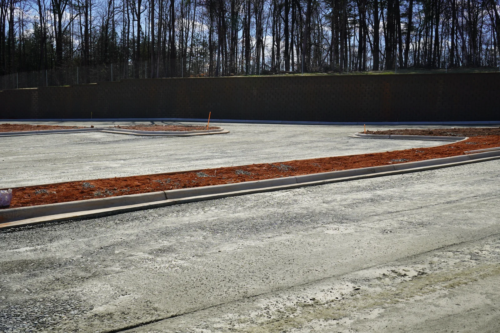Concrete pad installation with curbing, drainage pipe, and mulch base materials on wooded site