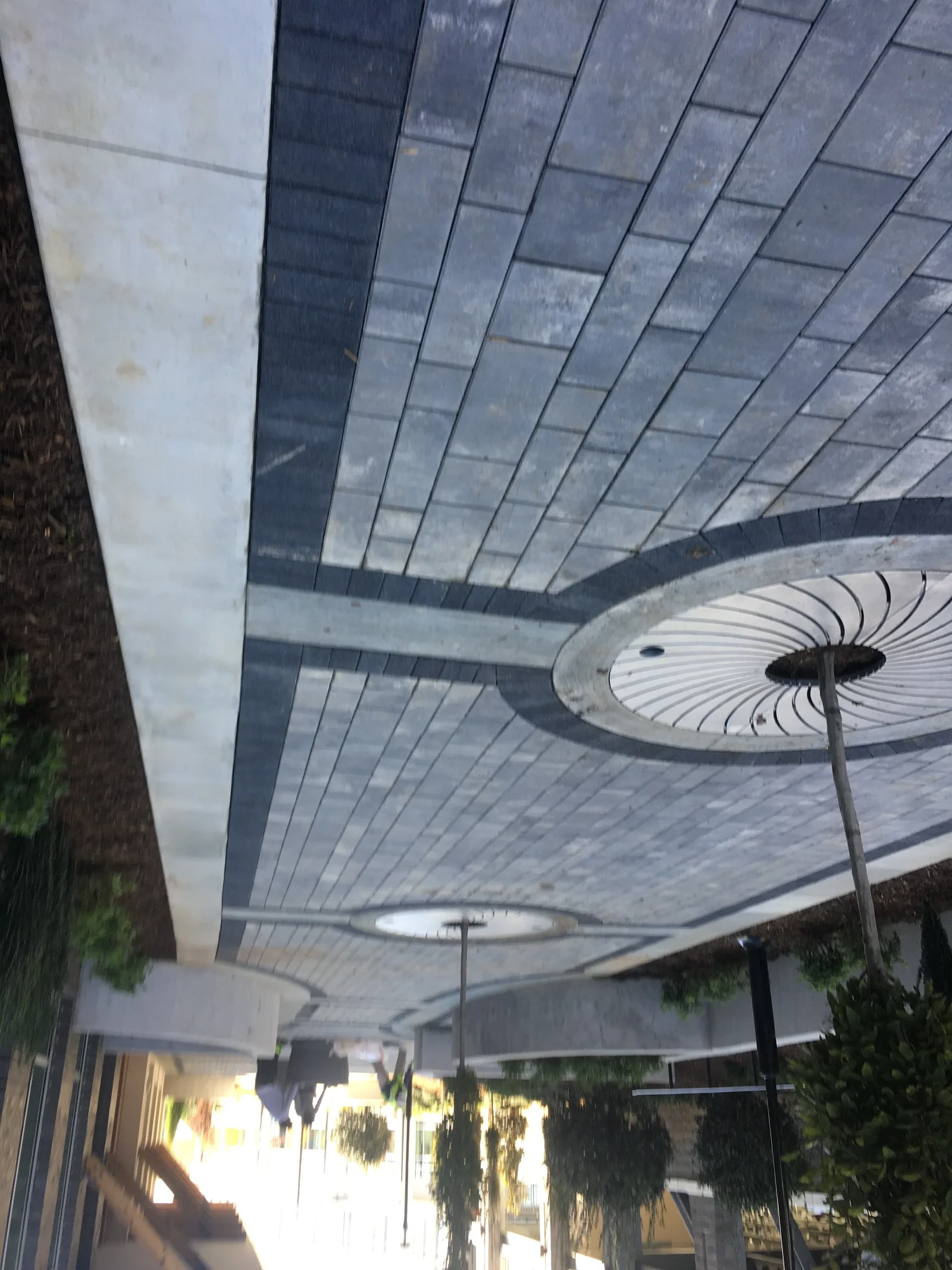 Herringbone pattern asphalt paving with dark and light strips, overhead lighting fixtures, curved design elements