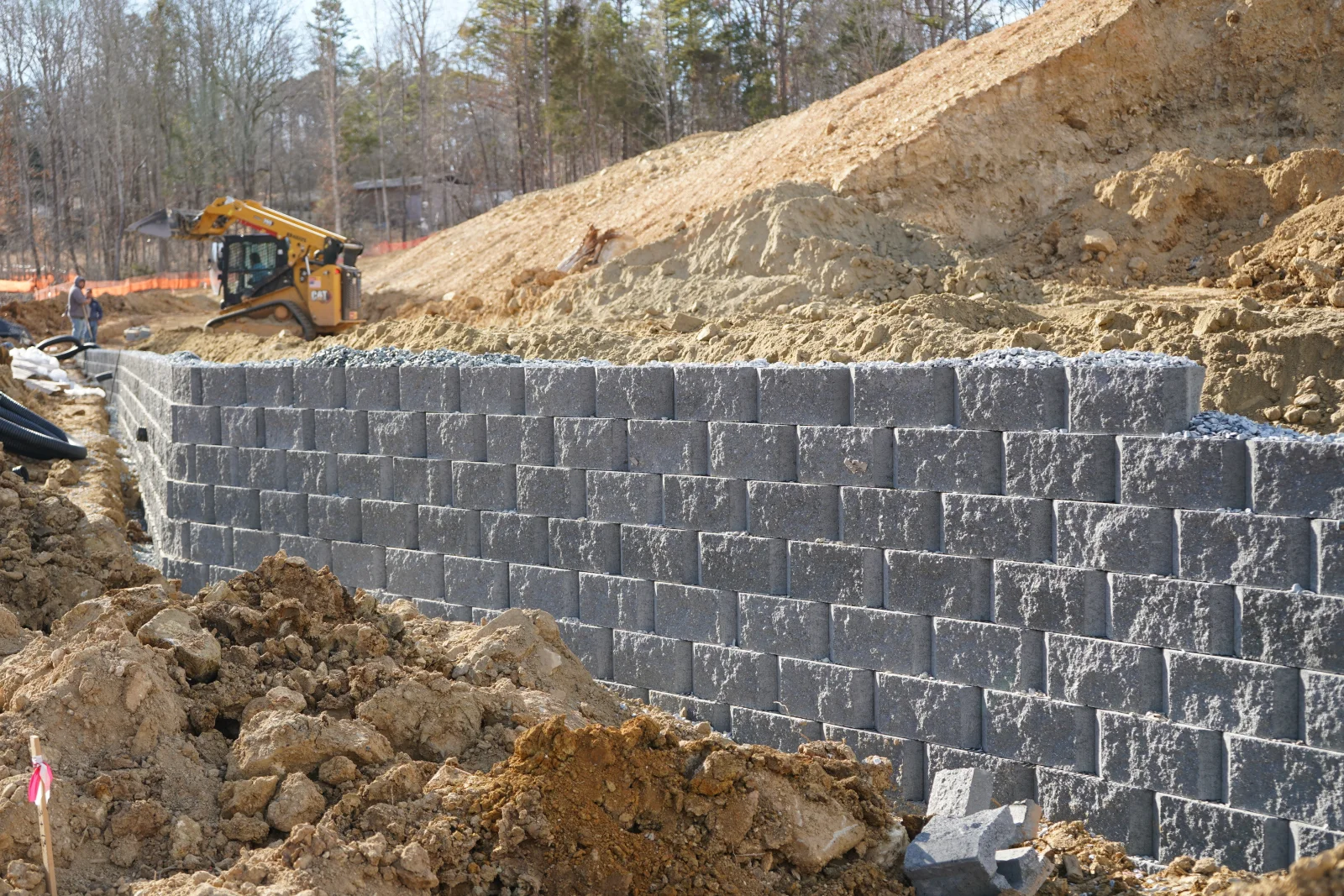 Gray segmental concrete retaining wall with multiple courses, compacted fill, and grading equipment on site
