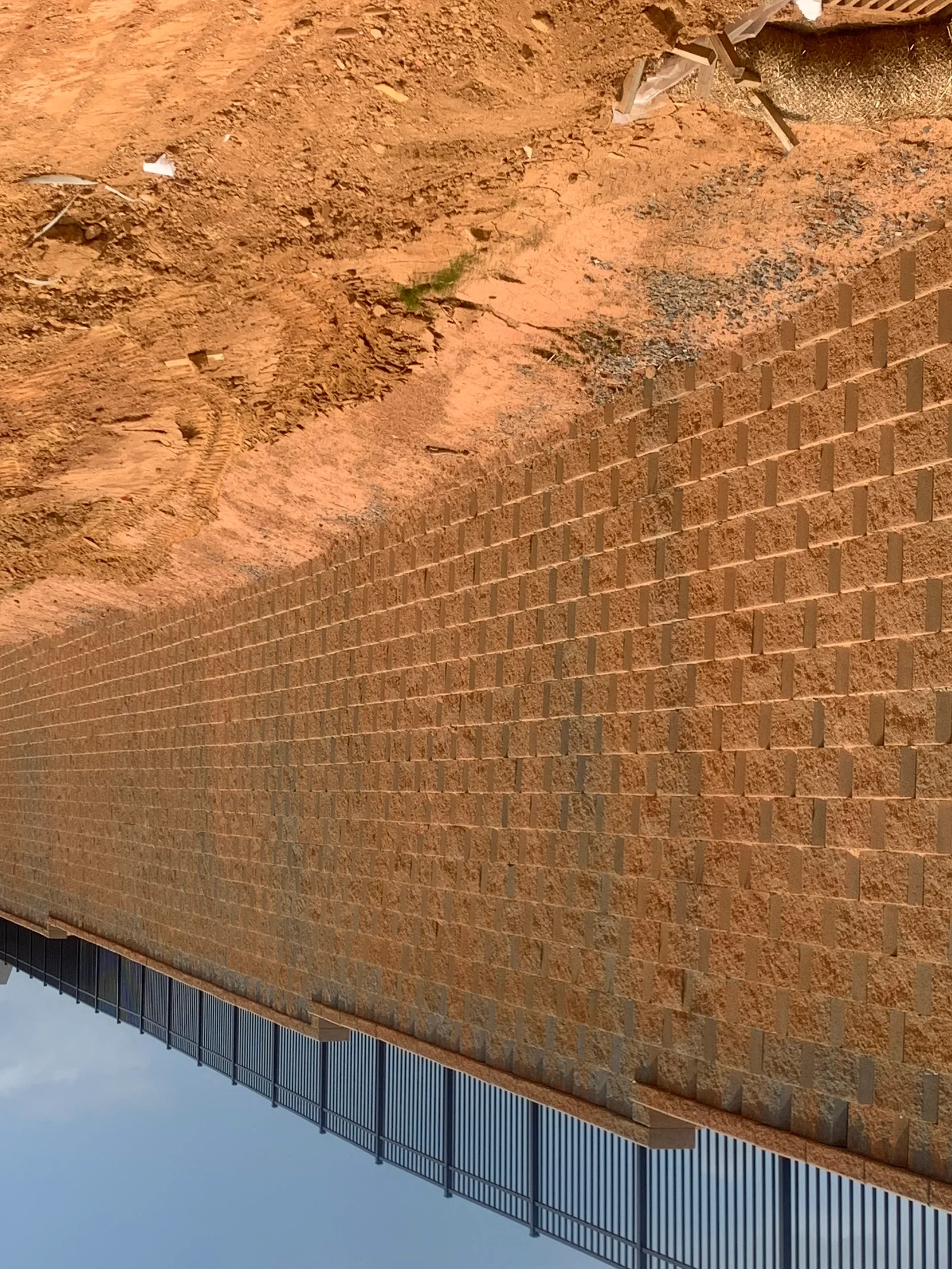 Tan segmental concrete retaining wall with metal reinforcement fencing at base